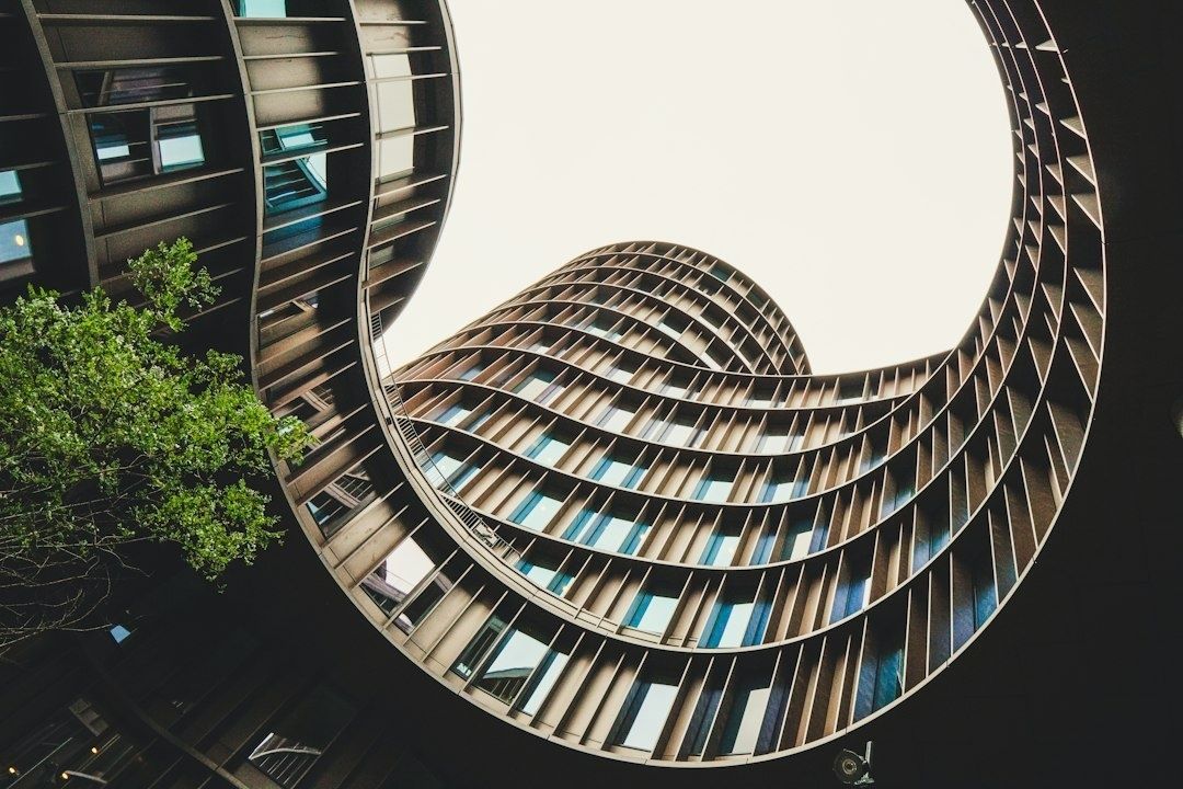 Böljande stadsbyggnad med fasader, fönster och ett träd sett underifrån